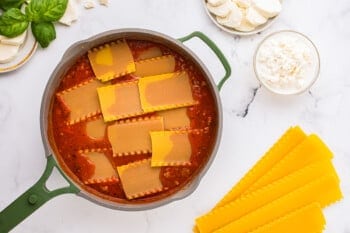 A pan of ravioli with sauce and cheese on a marble table.