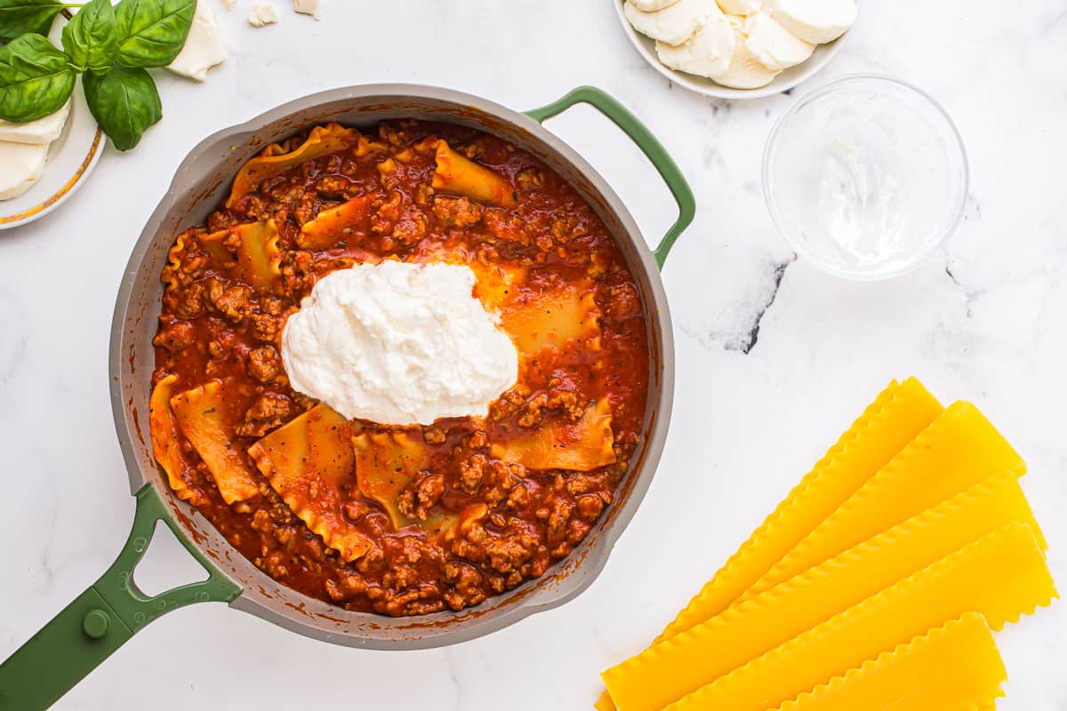 A heap of ricotta cheese on top of a noodles, meat, and tomato sauce in a pan.