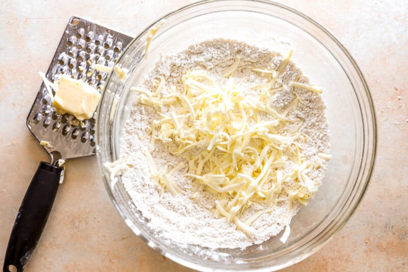 A bowl of shredded cheese and a grater next to it.