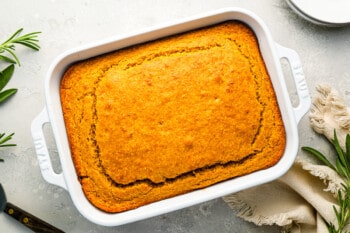 Cornbread in a white baking dish with sprigs of rosemary.