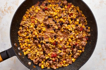 A frying pan filled with corn, beans and meat.