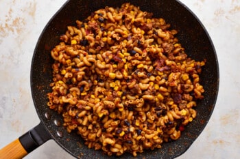 A frying pan filled with pasta and corn.