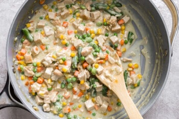 Chicken and peas in a pan with a wooden spoon.