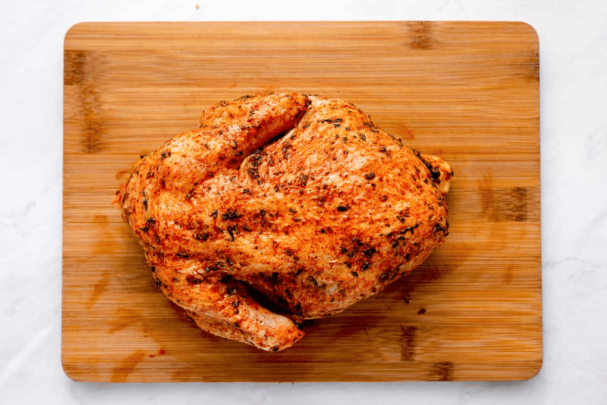 Seasoned whole chicken on a wooden cutting board.