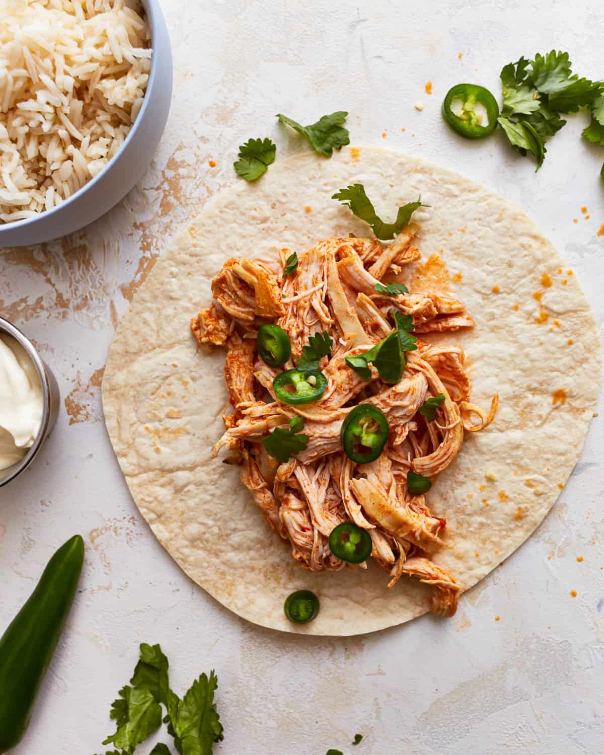 Instant pot shredded chicken spread onto a tortilla with sliced jalapeños, to make tacos.