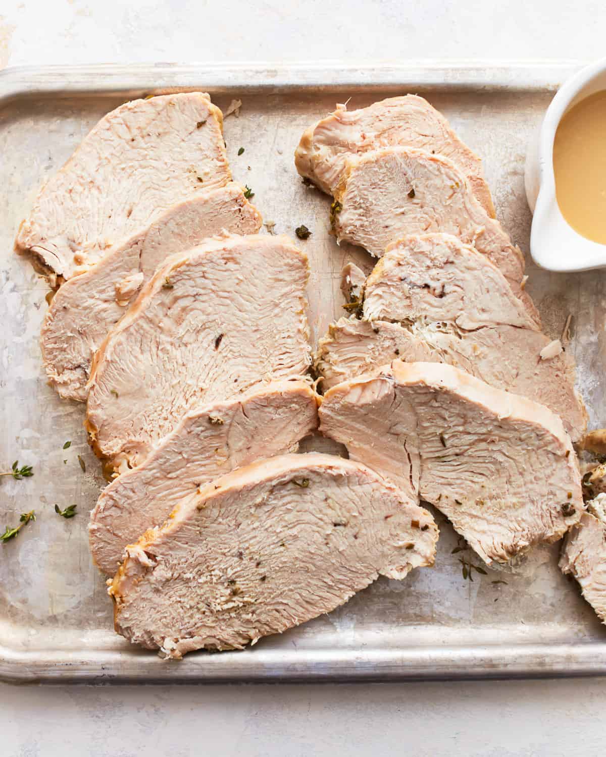 Slices of pressure cooker turkey breast on a baking sheet with a dish full of turkey gravy.
