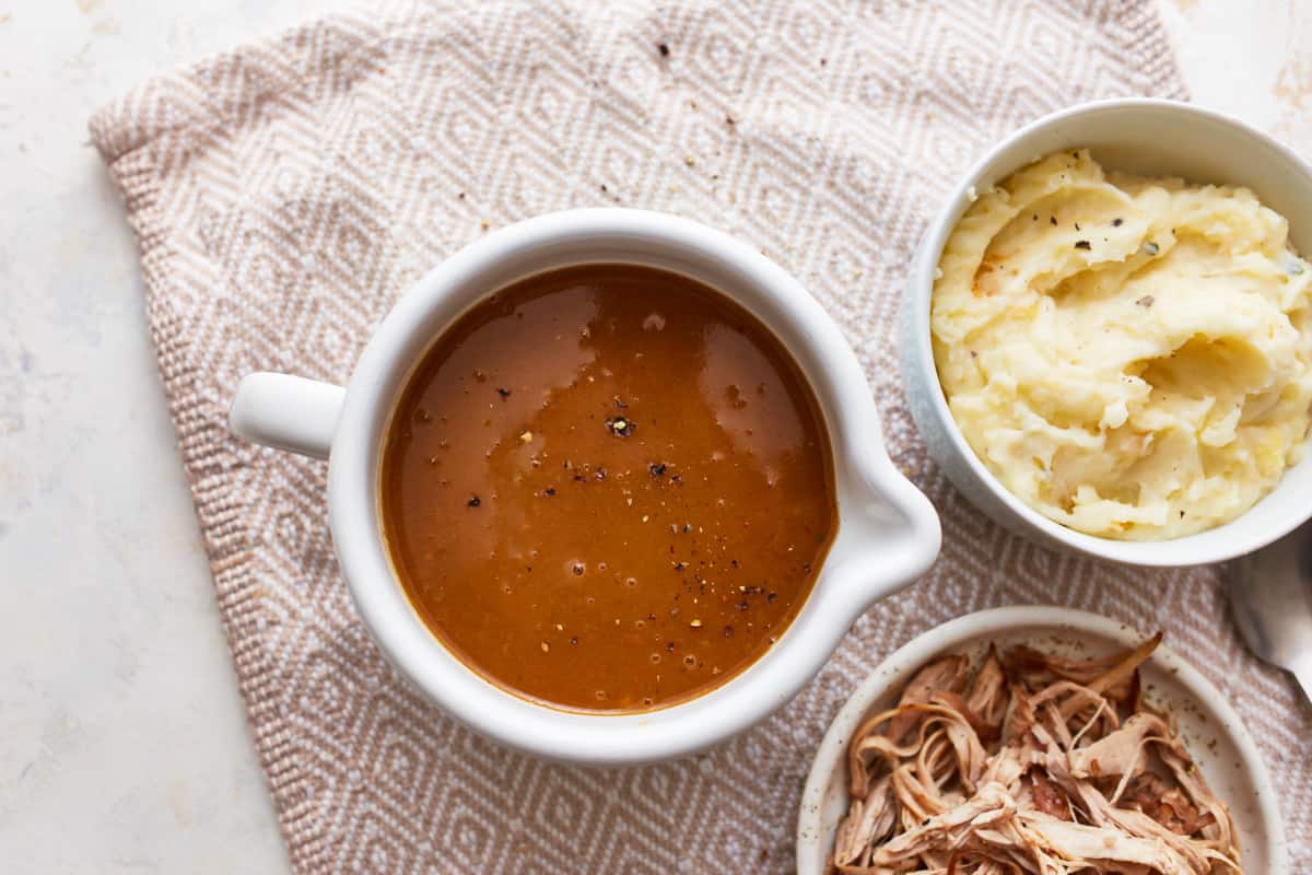 A bowl of make ahead gravy on a table with dishes full of mashed potatoes and turkey.
