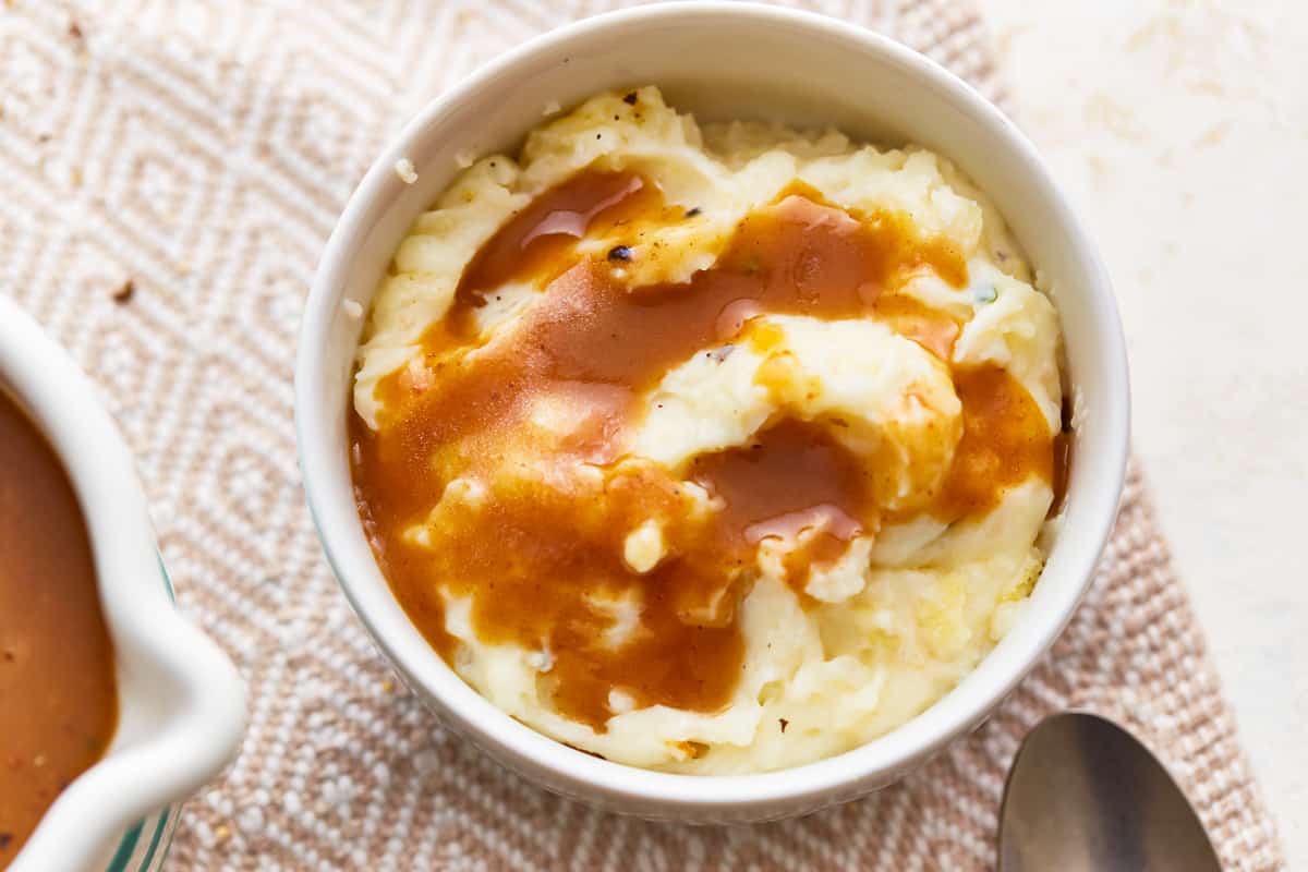 A bowl of mashed potatoes with gravy and a spoon.