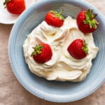 A blue plate with whipped cream and strawberries.