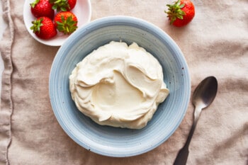 A bowl of mascarpone cheese with strawberries and a spoon.