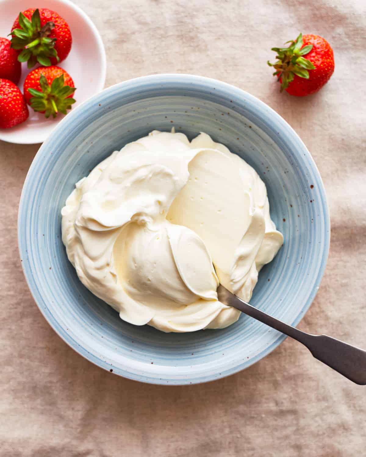 A bowl of mascarpone cream cheese, with strawberries around it.