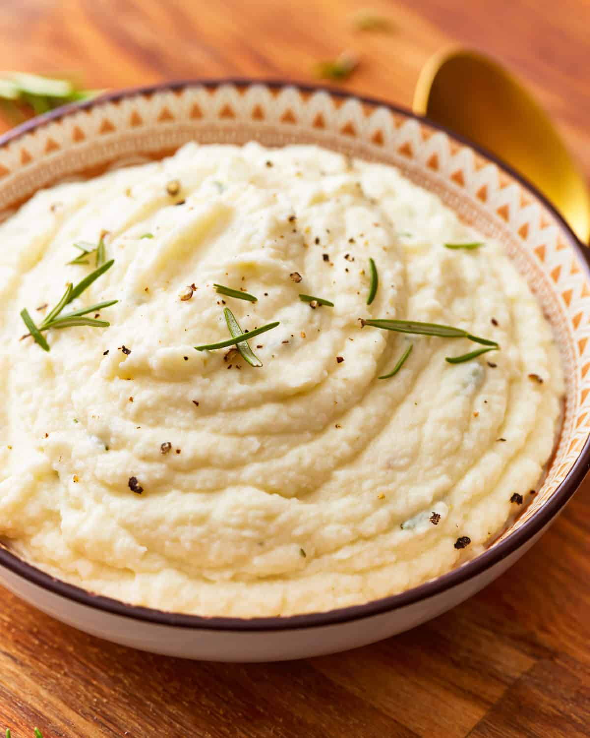 A bowl of mashed cauliflower with sprigs of rosemary.