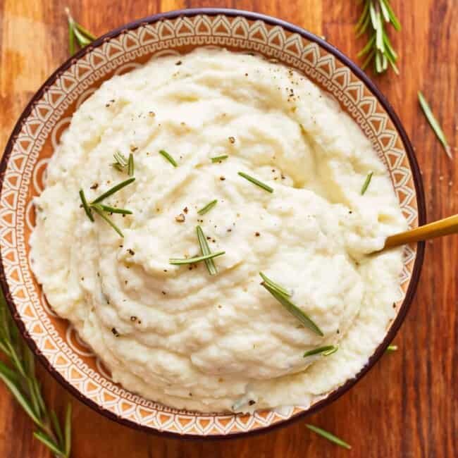 Mashed potatoes in a bowl with rosemary sprigs.