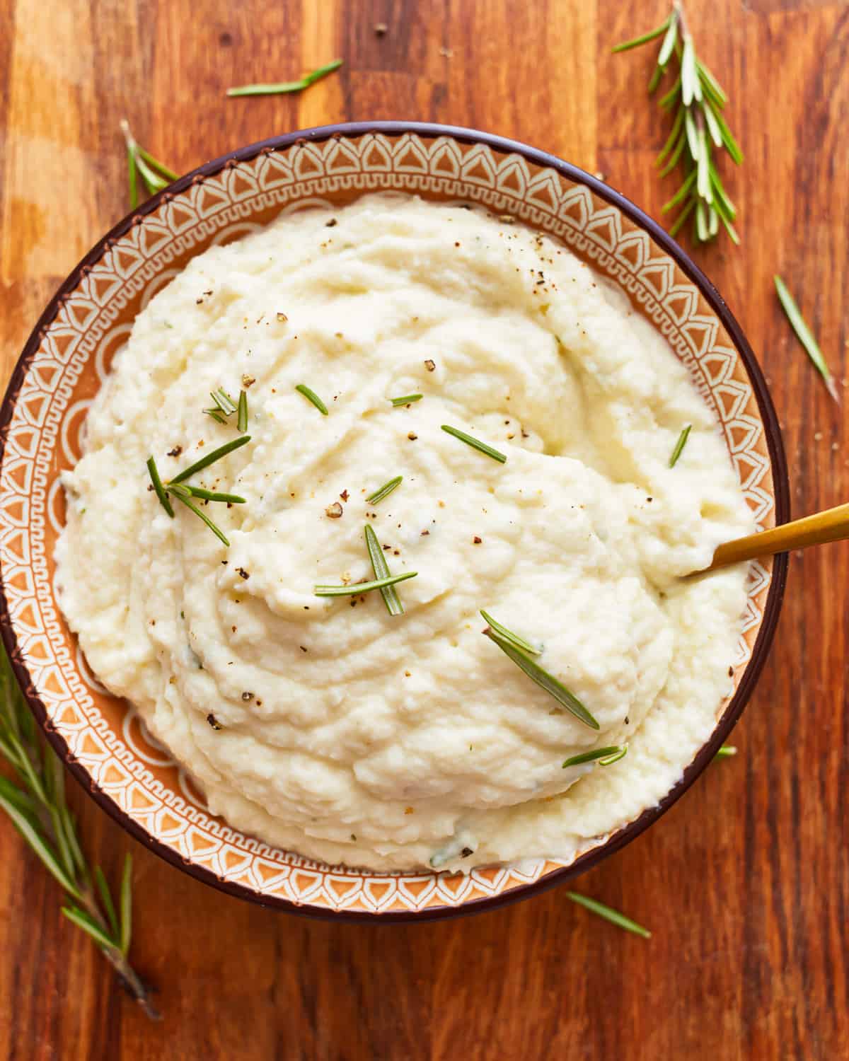 Mashed cauliflower in a bowl with rosemary sprigs.