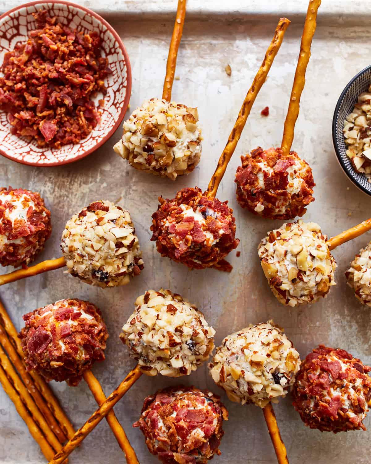 A tray of cheese ball bites on pretzel sticks, coated in bacon and chopped nuts.