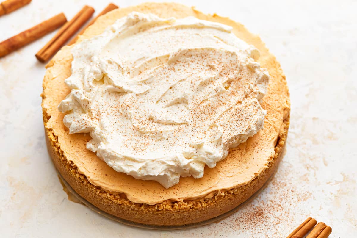 A no bake pumpkin cheesecake topped with whipped cream and cinnamon sticks.