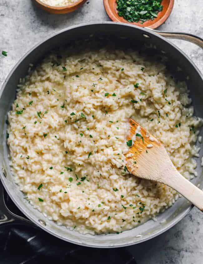parmesan risotto in a sautépan with a wooden spoon.
