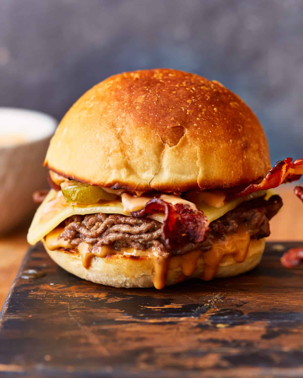 A burger with bacon and cheese on a cutting board.