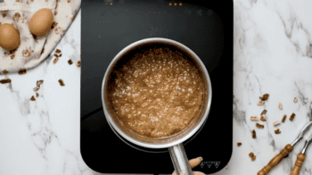A person stirs brown sugar in a pan while preparing a Classic Pecan Pie.