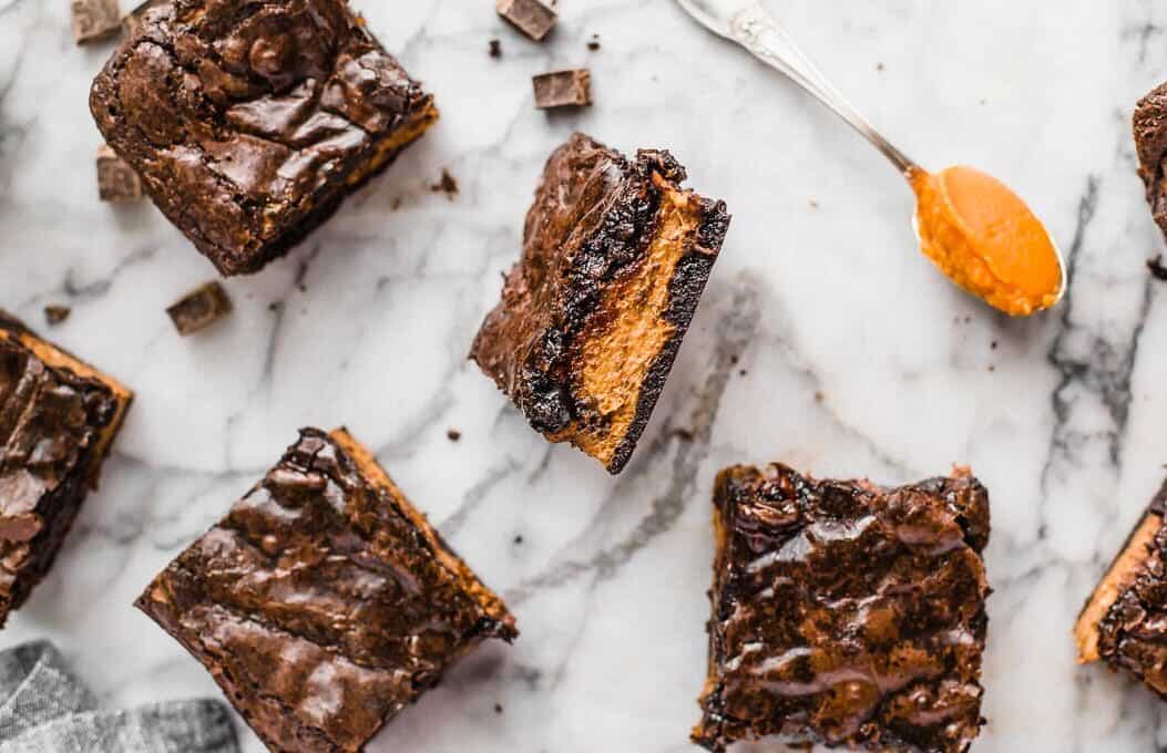 Pumpkin Brownies are an easy fall dessert recipe perfect for Halloween or Thanksgiving. Add a layer of pumpkin to your brownies for something fun and delicious! overhead view of brownies scattered on a marble countertop, one upturned to show a pumpkin layer.