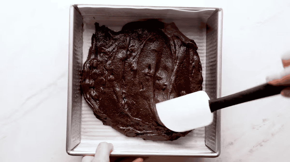 Spreading brownie batter in the bottom of a square baking pan with a rubber spatula.