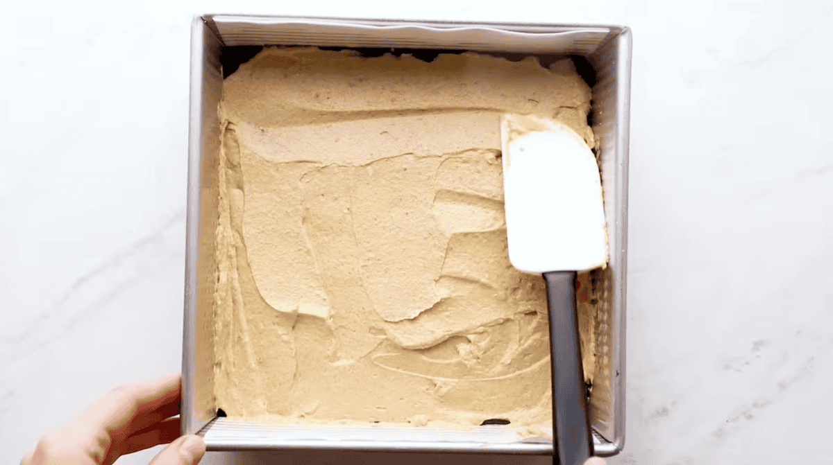 Spreading pumpkin filling over brownie batter in a square pan with a rubber spatula.
