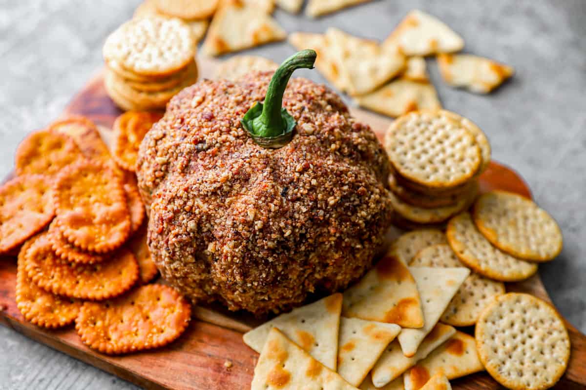 A pumpkin cheese ball with a variety of crackers on a serving board.
