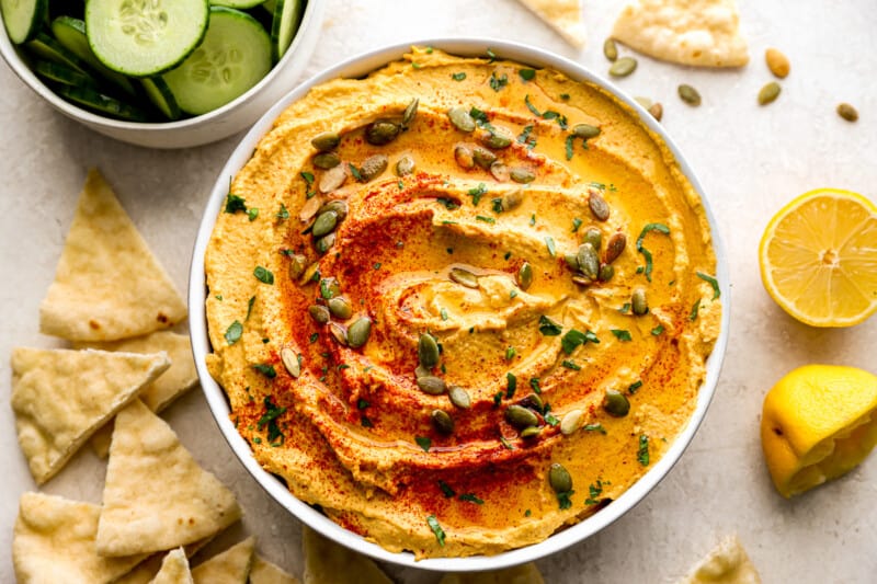 A bowl of hummus with pita chips and cucumbers.