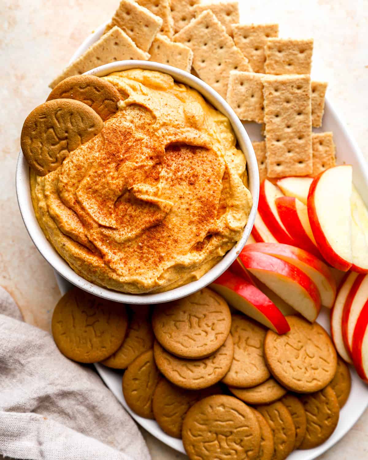 A bowl of pumpkin dip with crackers and apples.