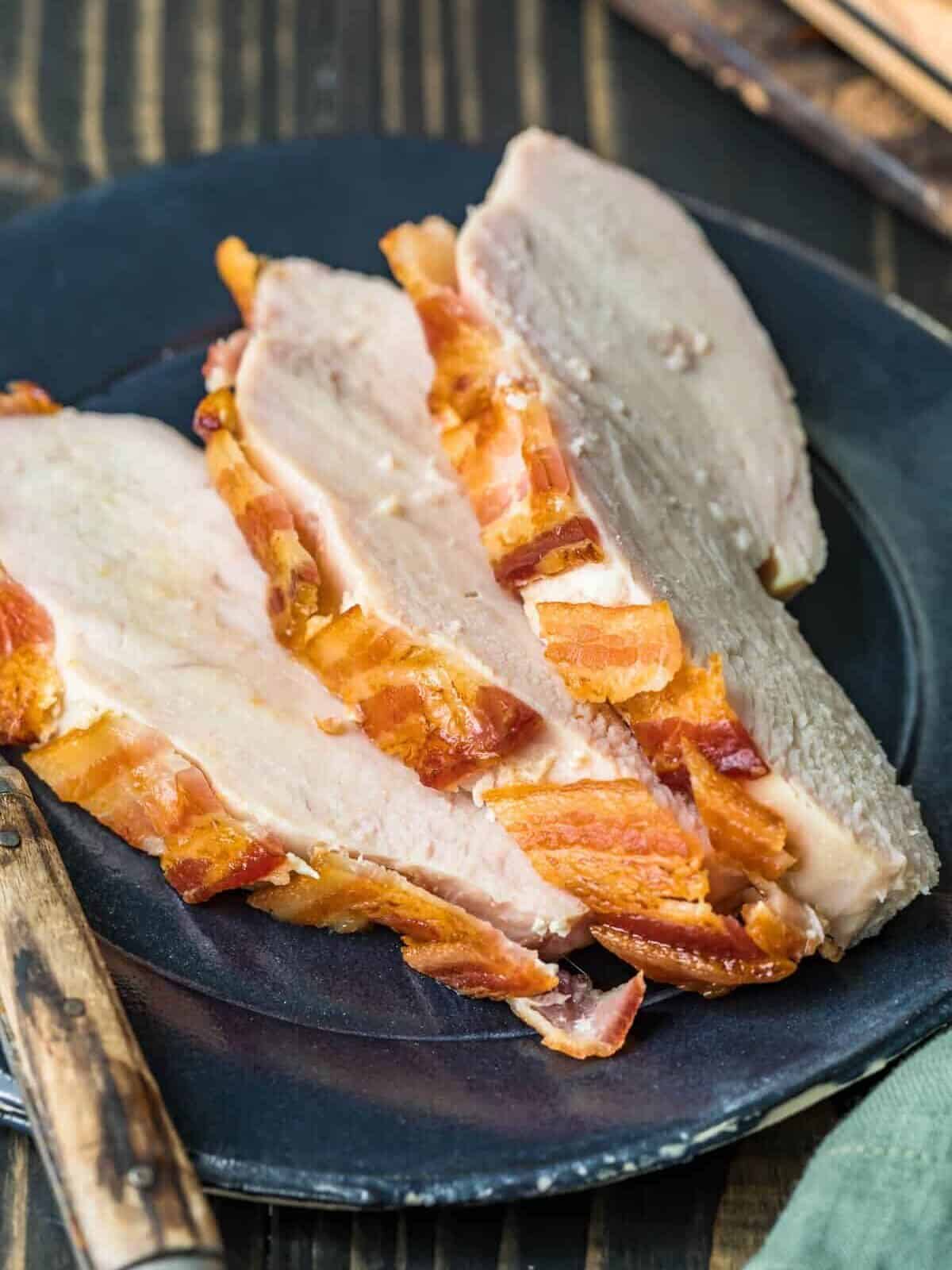 Sliced bacon on a plate next to a knife, served alongside Pasta Pomodoro.