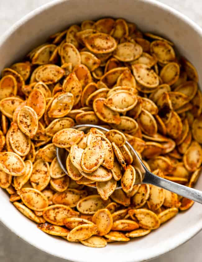 Pumpkin seeds in a white bowl with a spoon.