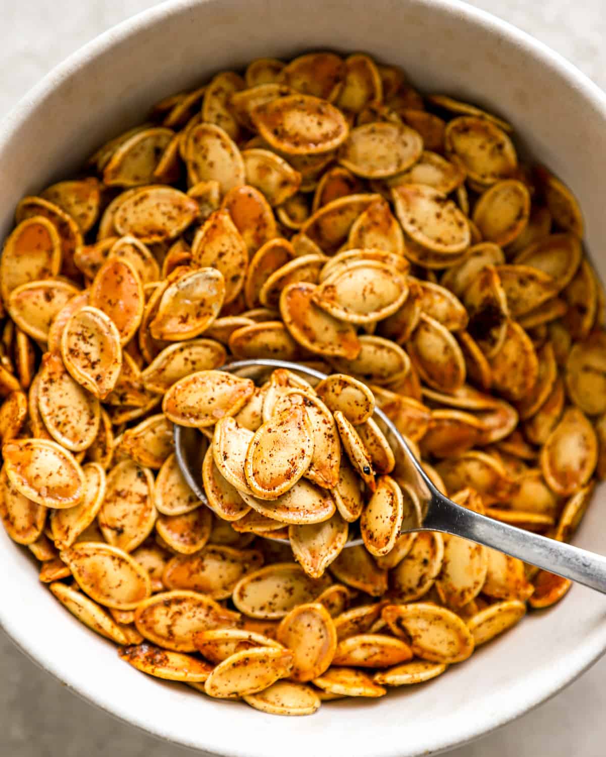 Roasted pumpkin seeds in a white bowl with a spoon.