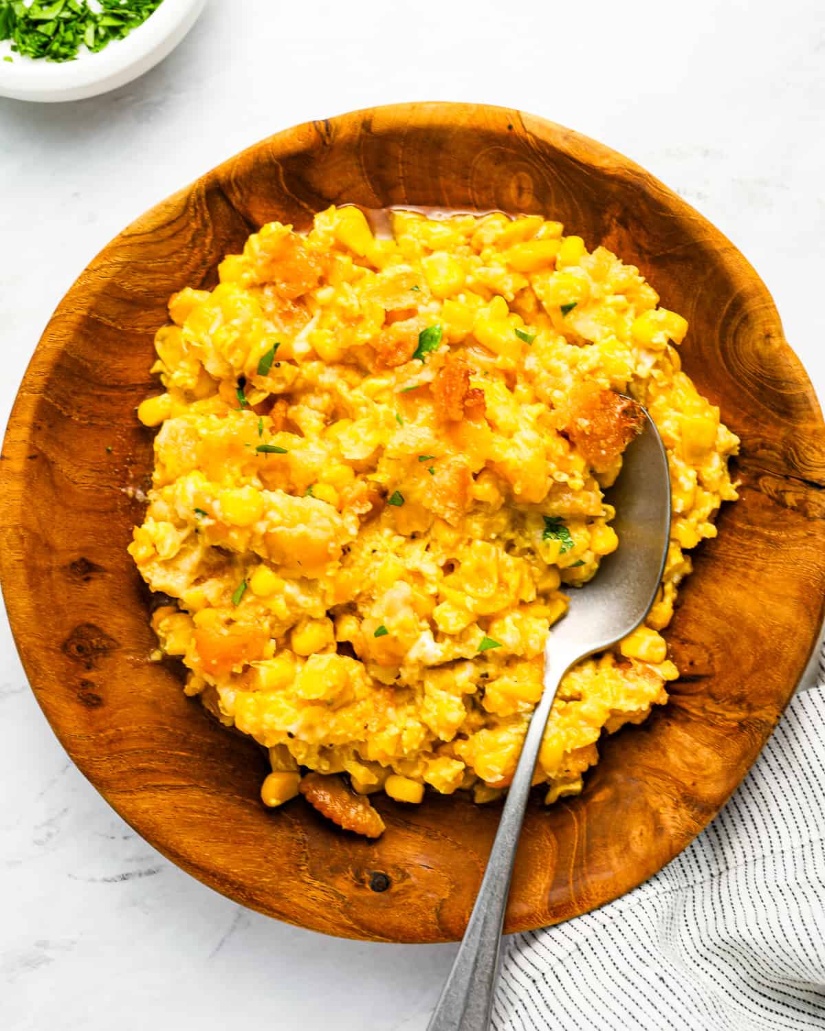 A serving of scalloped corn in a wooden bowl with a spoon.