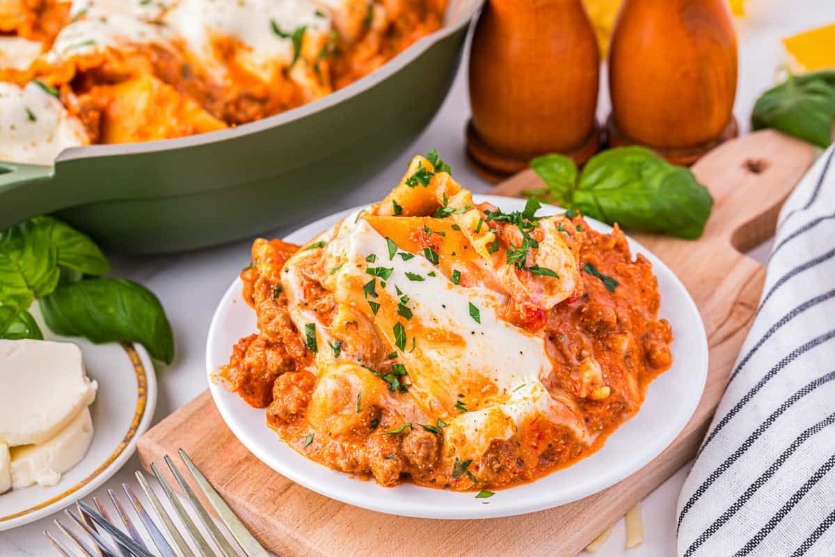 A plate of lasagna with meat and cheese on a wooden cutting board.