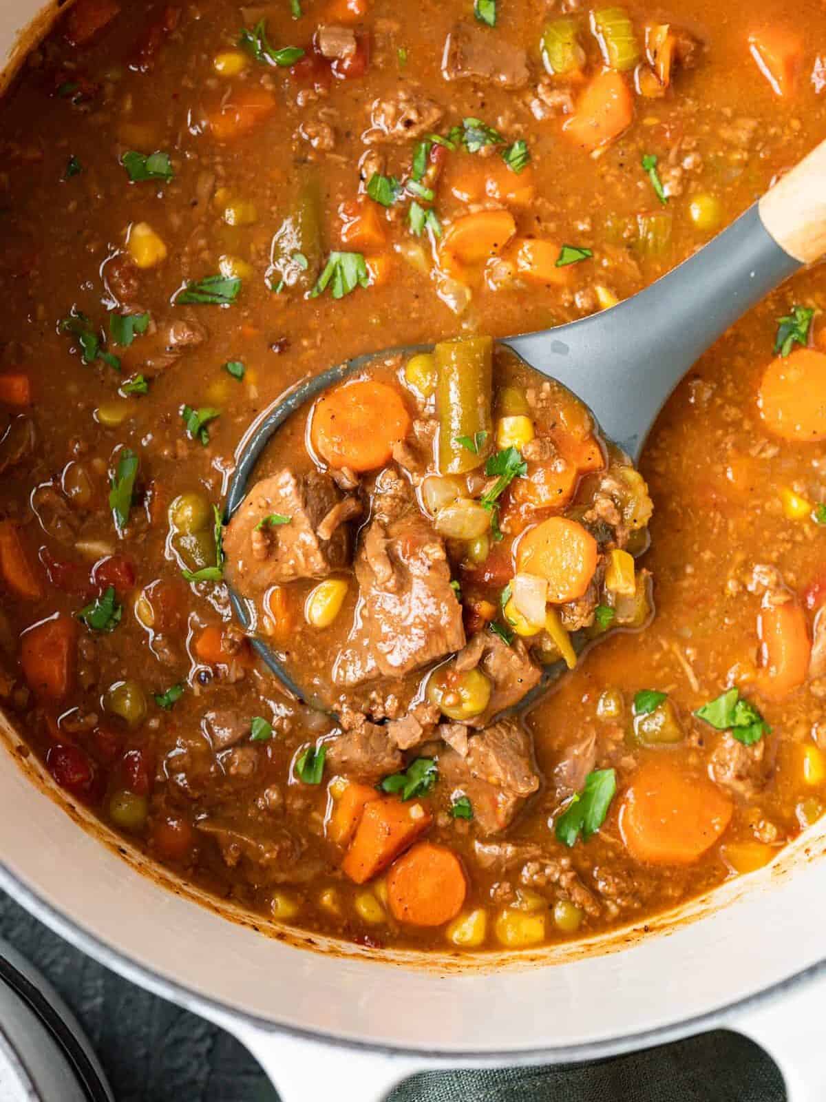 overhead view of steak soup in a dutch oven with a serving spoon.