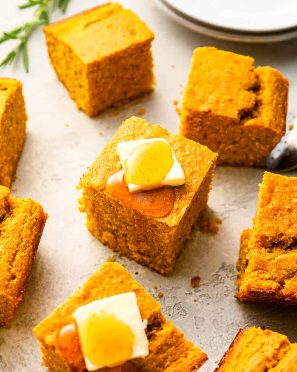 Sweet potato cornbread squares with butter and honey on a plate.