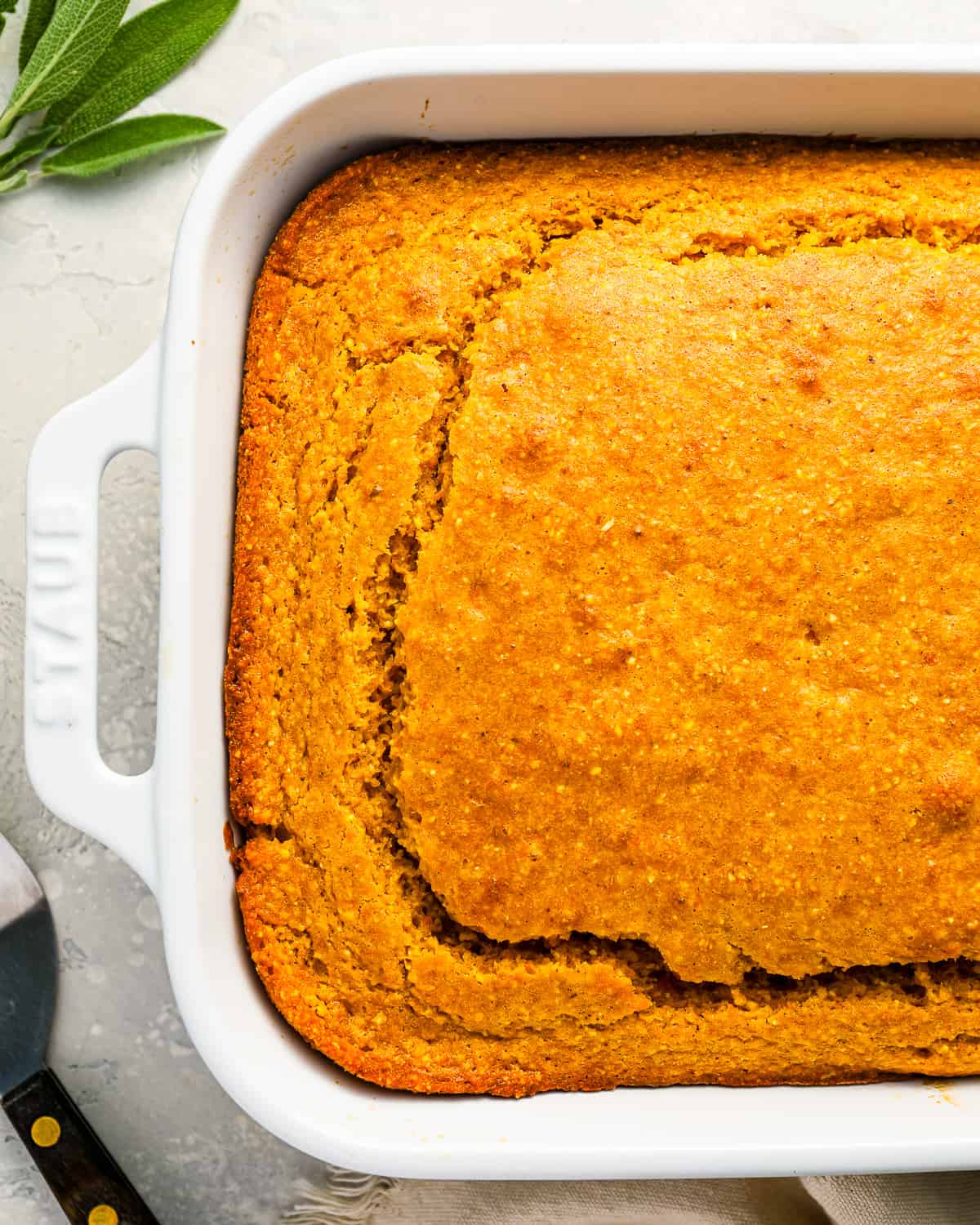 Cornbread bread in a white baking dish with sprigs of sage.