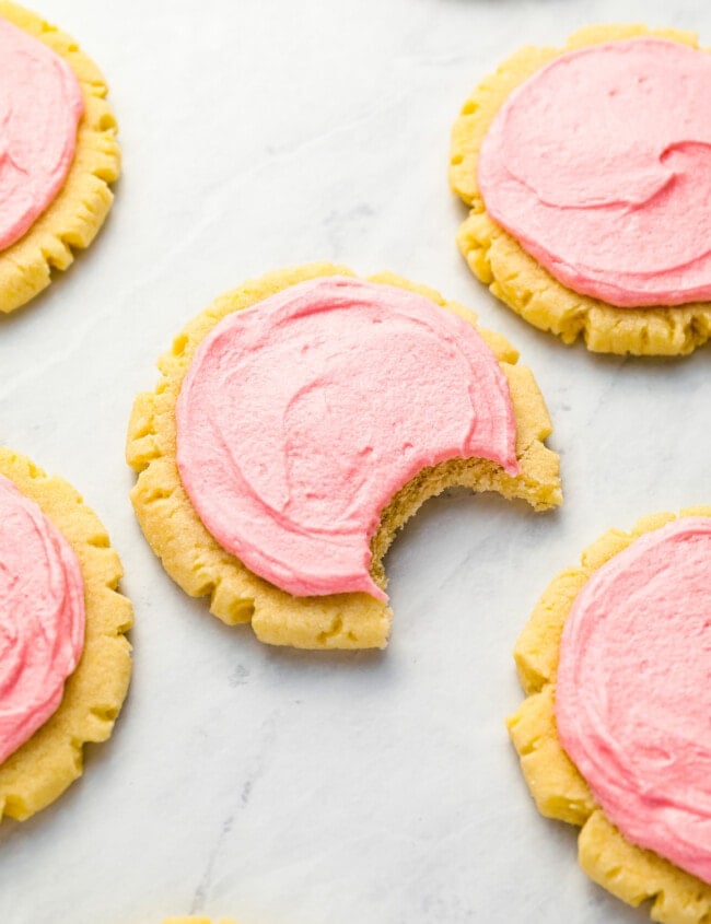 Pink frosted cookies with a bite taken out of them.