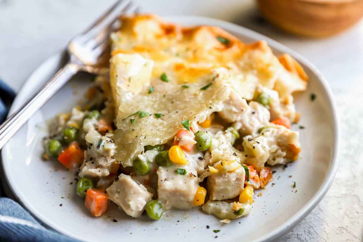 A slice of leftover turkey pot pie on a white plate with a fork.