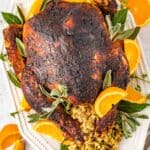 overhead view of dry brined turkey n a white serving dish with sliced oranges and herbs.