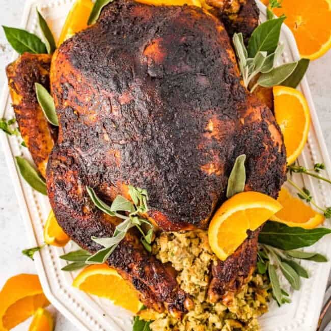 overhead view of dry brined turkey n a white serving dish with sliced oranges and herbs.