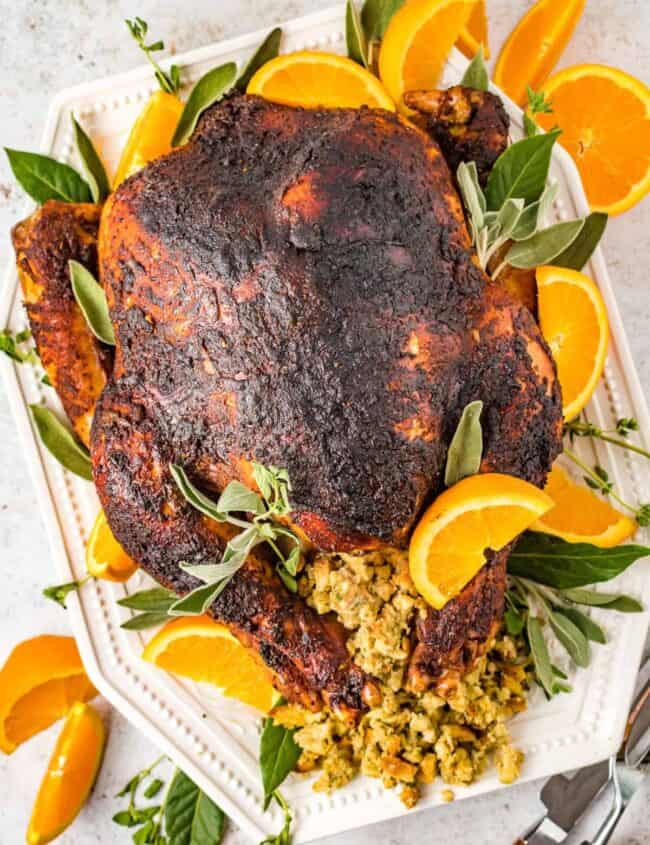 overhead view of dry brined turkey n a white serving dish with sliced oranges and herbs.