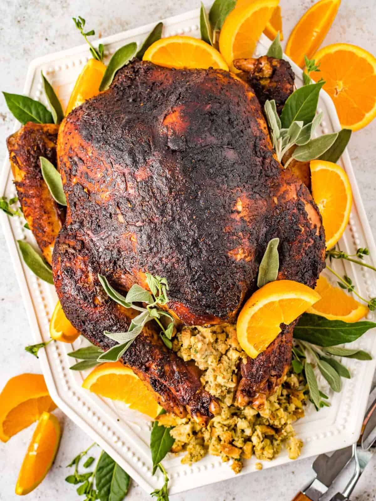 overhead view of dry brined turkey n a white serving dish with sliced oranges stuffing and herbs.