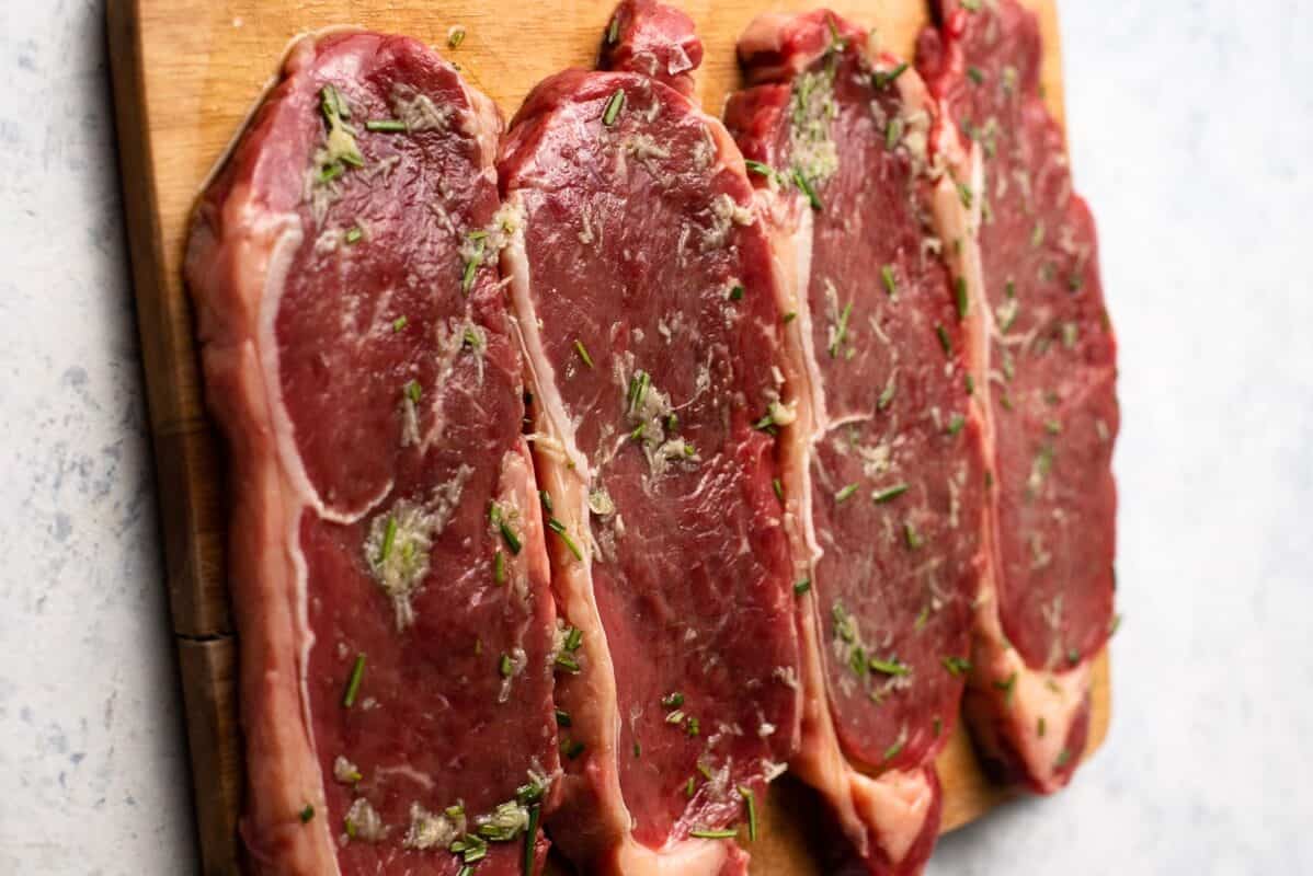 New York strip steaks beautifully arranged with herbs on a cutting board.