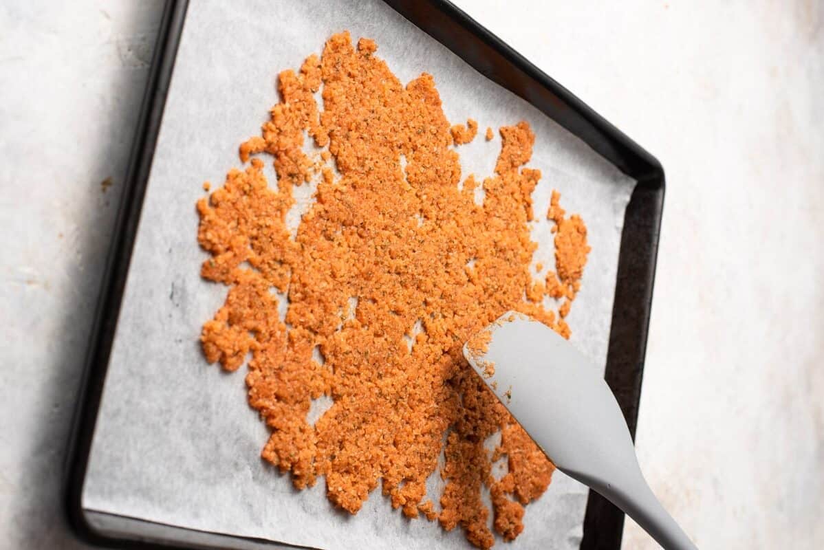 a spatula is being used to stir a batch of granola on a baking sheet.
