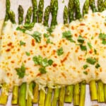 A tray of asparagus gratin topped with cheese and parsley.