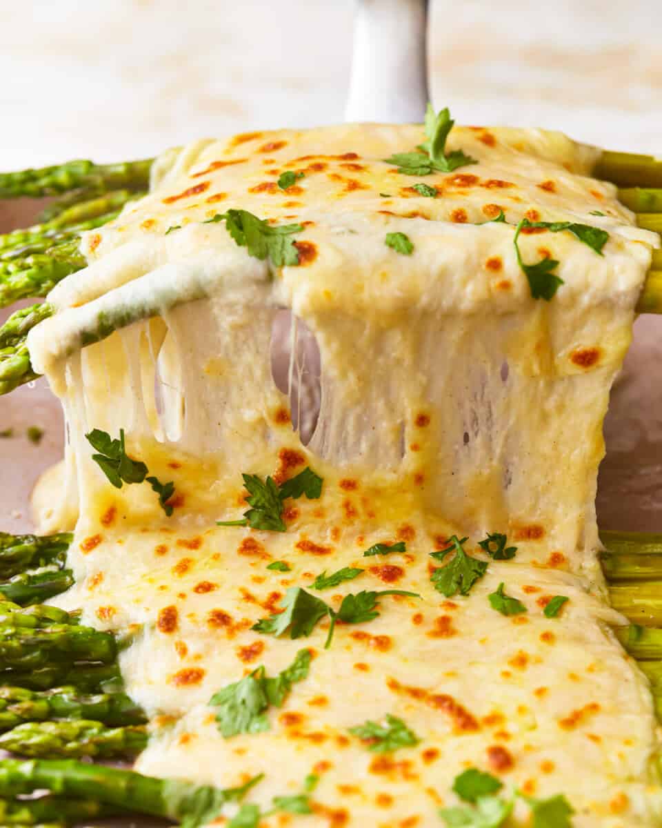 Spatula lifting stalks of asparagus in a thick cheese sauce.