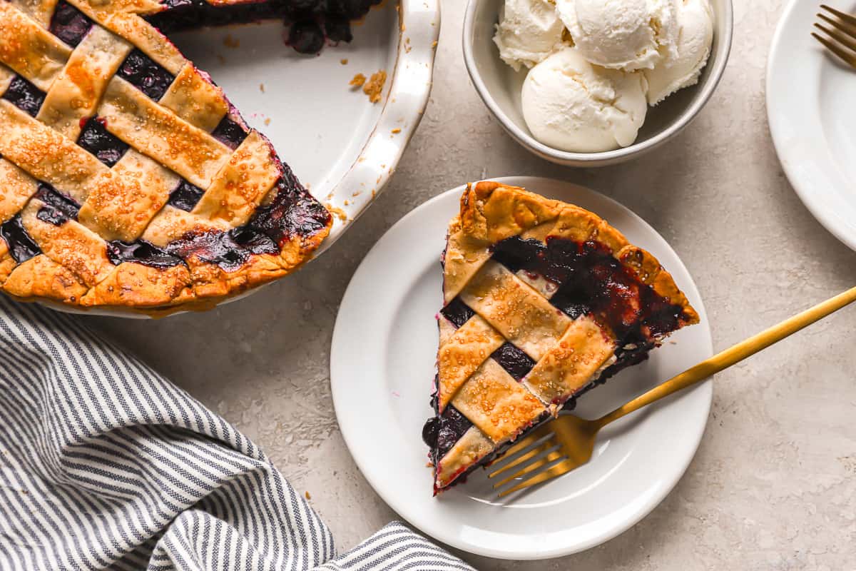 A slice of fresh blueberry pie with ice cream on a plate.