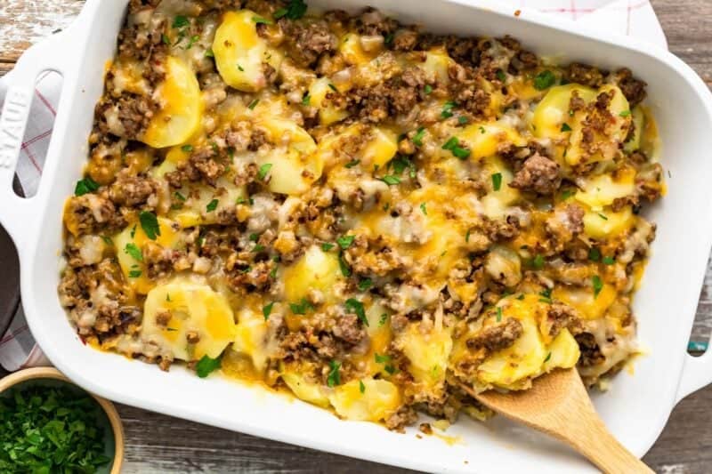 Sausage and potato casserole cooked in a baking dish with a wooden spoon.