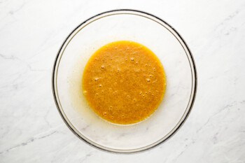 Orange sauce in a glass bowl on a marble surface.